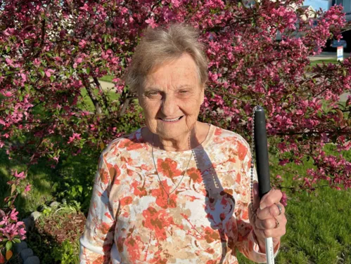 An older woman standing in of a tree that has pink blooming flowers.
