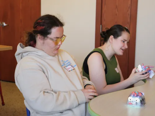 Two girls sitting at a table playing with small interactive robots