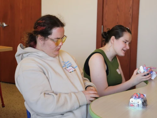 Two girls sitting at a table playing with small interactive robots