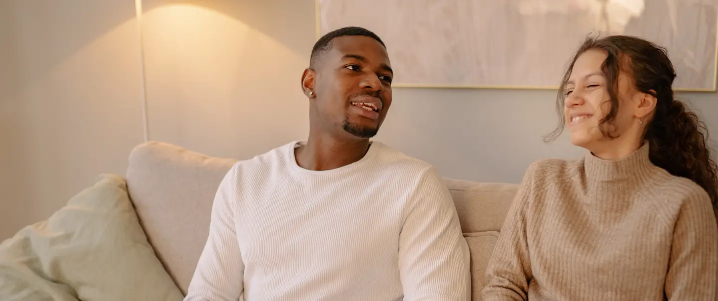 Man in white sweater reading Braille book while girl smiles next to him