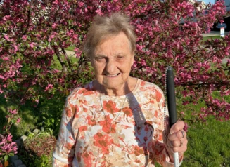 An older woman standing in of a tree that has pink blooming flowers.