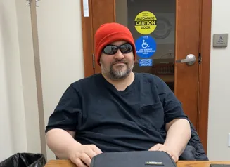 A man in a red beanie and sunglasses sits at a table in a small room.