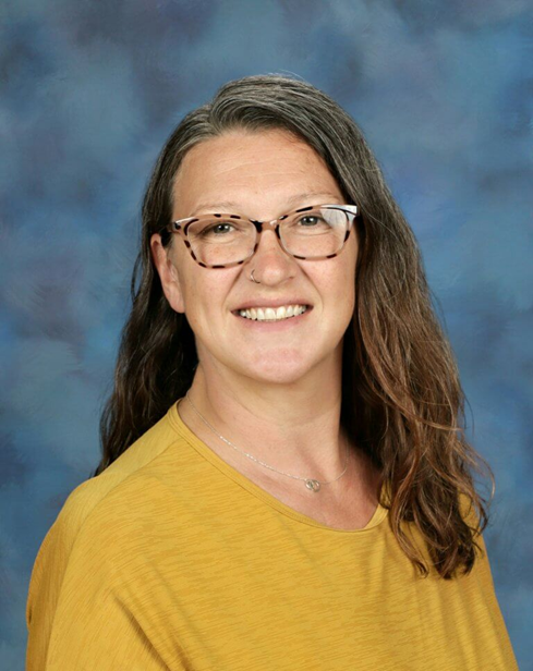 A professional headshot of a woman with shoulder length brown hair and glasses smiling and wearing a yellow shirt